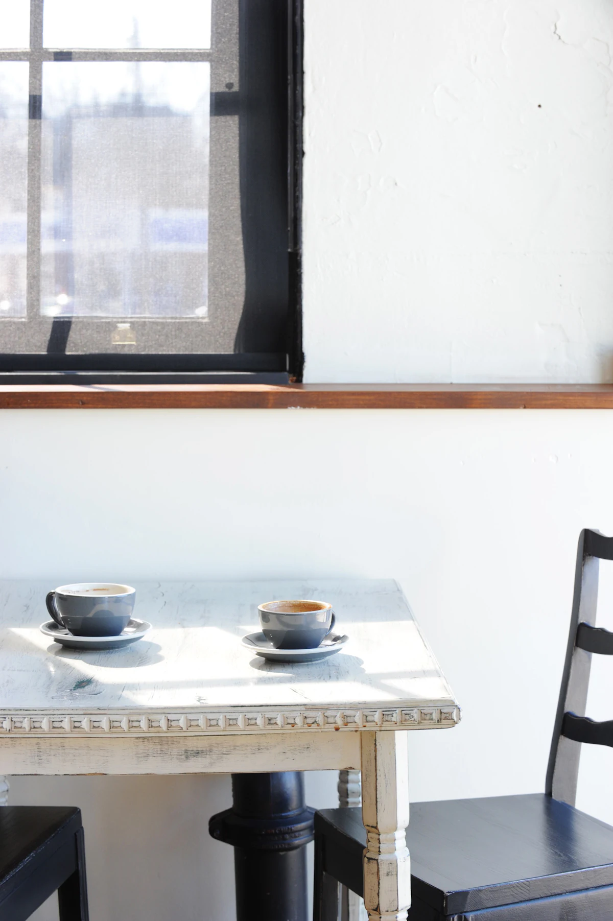 Dos tazas de café sobre una mesa junto a una ventana con luz de la mañana